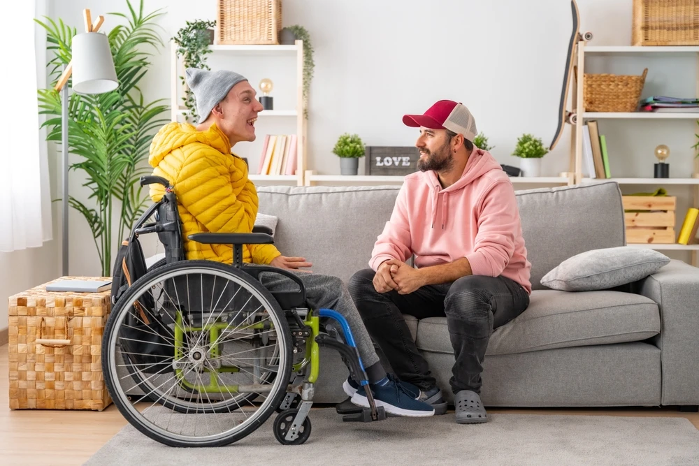 Disabled man in wheelchair talking with support worker on couch